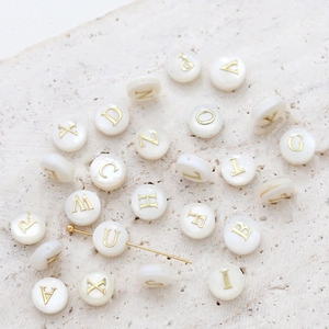 Macro shot of natural shell alphabet beads with gold letter engraving for jewelry DIY