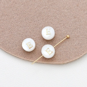 Macro detail of 8mm shell bead with golden letter E for DIY jewelry crafting