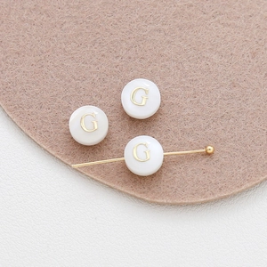 Macro detail of 8mm round shell alphabet bead with golden letter G for DIY jewelry making