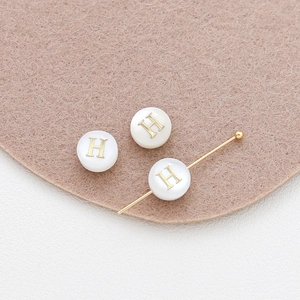Detailed close-up of 8mm round white shell beads with golden H letter for DIY jewelry