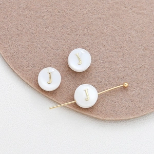 Detailed macro view of 8mm shell beads with gold letter J for DIY bracelet jewelry making