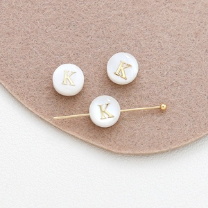 Macro detail of white shell beads featuring a gold letter K for DIY jewelry crafting