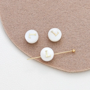 Macro detail of white shell alphabet beads with gold letter L for DIY jewelry making