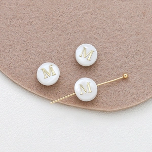 Close-up of 8mm natural shell bead with golden letter M for DIY jewelry making