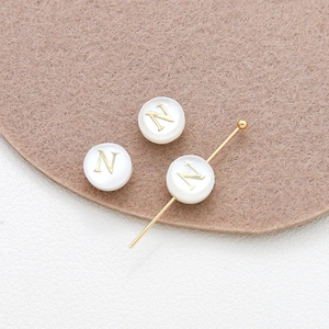 Macro shot of 8mm natural shell beads with gold letter N for DIY jewelry making