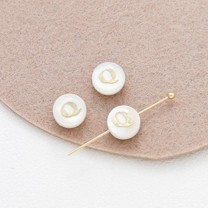 Macro detail of 8mm shell beads with gold letter Q and T-pin for DIY jewelry making