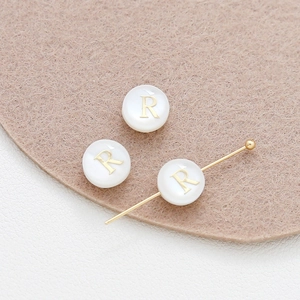 Detailed macro view of 8mm shell beads with golden letter R for DIY jewelry making