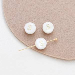 Close-up of 8mm natural shell round beads with golden letter S for DIY jewelry making