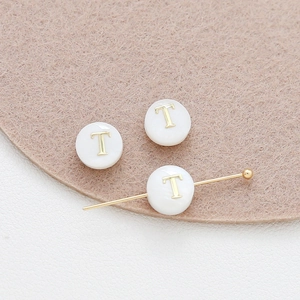 Macro view of 8mm round natural shell alphabet beads with gold letter T for DIY jewelry
