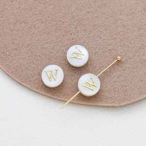 Macro detail of white shell alphabet beads with gold letter W for DIY jewelry