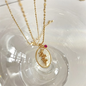 Detalle del colgante ovalado dorado con relieve floral de nácar y una gema roja