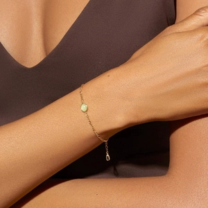 Close-up of a green aventurine gemstone pendant on a gold Figaro chain bracelet