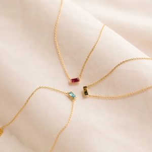 Close-up of gold titanium necklaces with rectangular garnet, blue and green zircon pendants