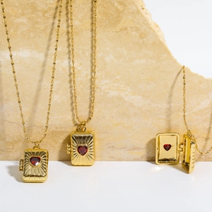 Detail view of heart-shaped gold locket necklace featuring a red gem and engraved lines