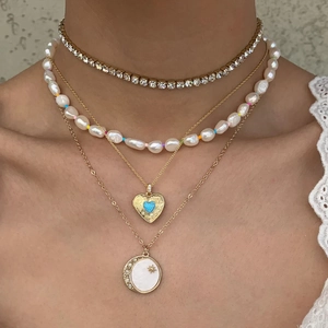 Layered gold necklace set featuring heart locket, pearls and blue gemstone pendant