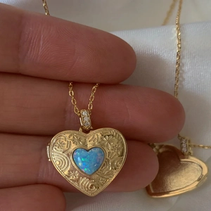 Gold locket necklace with floral engraving and blue heart opal on white satin cloth