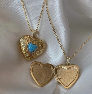 Detailed macro of gold heart locket necklace with vintage floral engraving and blue opal