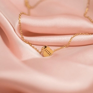 Macro detail of gold heart pendant with 11:11 engraving on soft pink satin fabric