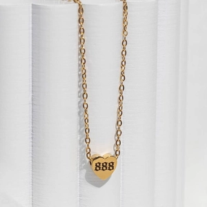 Detail of gold heart pendant with 888 engraving on a white display column
