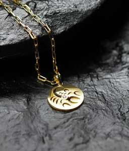 Macro shot of gold zodiac necklace with Scorpio pendant on a black rock surface