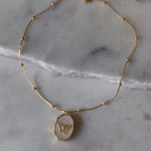 Collier médaillon vintage plaqué or avec papillon et nacre sur un support en marbre