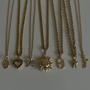 Set de collares dorados con colgantes de Hamsa, corazón, mariposa, sol y Love sobre blanco