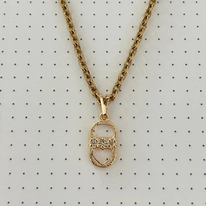 Detalle de colgante ovalado dorado con tres circonitas engastadas y calado de corazón