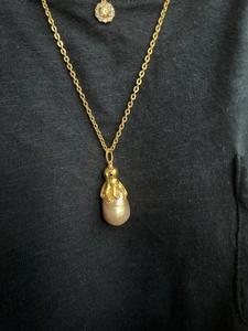 Detailed macro view of a golden octopus pendant holding a purple baroque pearl necklace