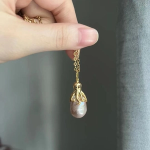 Macro shot of gold octopus pendant clutching a pink baroque pearl on a gold chain