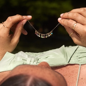 Golden birthstone necklace with multicolored gems and rings on model in nature