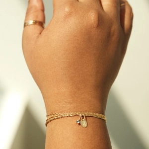 Detailed close-up of a layered gold chain bracelet with a letter A pendant and blue gemstone