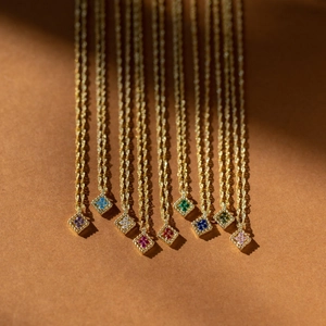 Close-up of golden square pendants with colorful zircon gemstones on brown texture