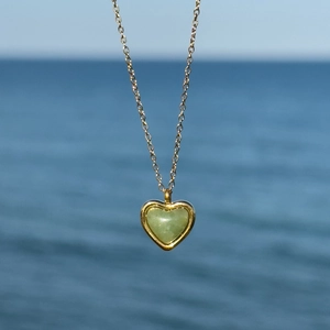 18K gold plated heart necklace with green agate stone pendant over a sea background
