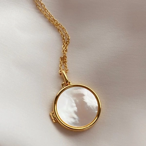 Dettaglio della collana con medaglione dorato e madreperla su sfondo di raso bianco puro