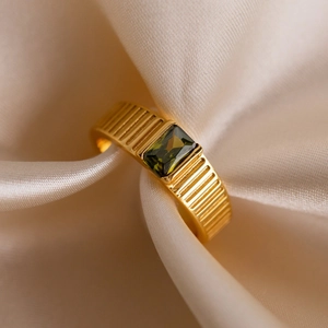 Detailopname van een smaragdgroene zirkoon op een getextureerde gouden ring op zijde