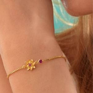 Pulsera de flor de loto dorada con circonitas rojas lucida en la muñeca femenina