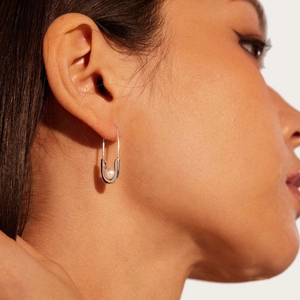 Detail view of a safety pin earring with a white pearl on a model's earlobe