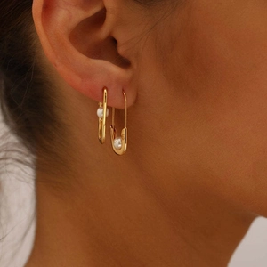 Close-up of a gold-plated pin-shaped earring with a white freshwater pearl on a model