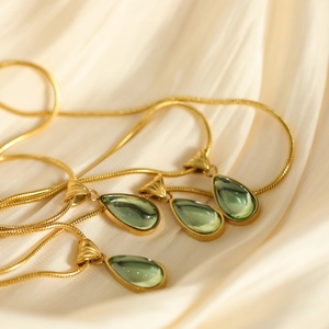 Elegante vergoldete Schlangenkette mit grünem Wassertropfen-Anhänger auf Seidenstoff
