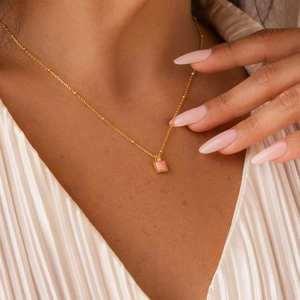 Dettaglio di una collana a sfere dorata con ciondolo a cuore in opale rosa su una modella