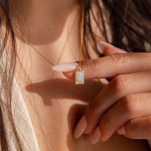Dettaglio di una collana in acciaio al titanio dorato con ciondolo rettangolare in opale rosa