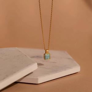 Dettaglio della collana quadrata dorata con opale cangiante su fondo marmo
