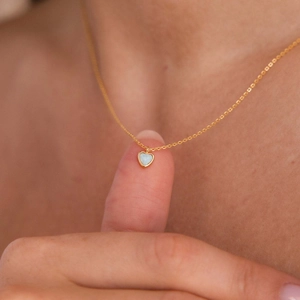 Dettaglio di un ciondolo a cuore in opale rosa su una collana in acciaio titanio dorato