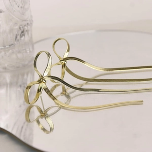 Dettaglio di orecchini a fiocco dorati con eleganti nappine a catena su base a specchio