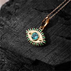 Makro-Detail der goldenen Evil Eye Halskette mit blauem Edelstein auf Holzkohle-Hintergrund