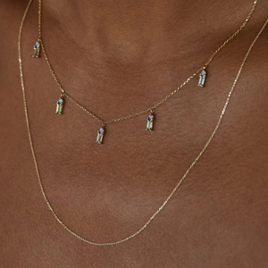 Close-up of layered gold necklaces featuring blue and opal teardrop pendant charms