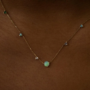 Detail of a gold double-layer necklace featuring small opals and emeralds on skin
