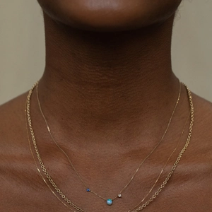 Close-up of layered gold necklaces featuring blue opal charms on dark skin background
