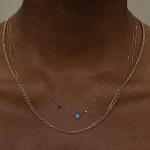 Gold layered necklace with round opal pendant and blue stone on female model
