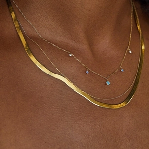Close-up of gold double-layered necklace with flat snake chain and blue opal pendants